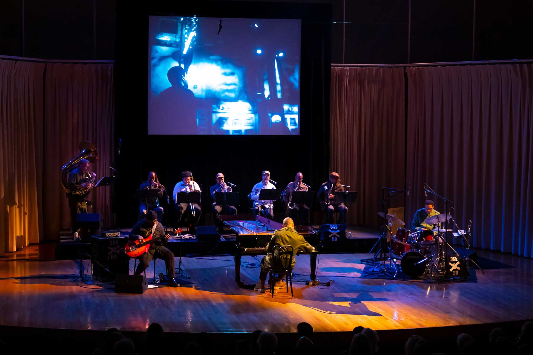 10 musicians playing piano, drums, wind and string instruments on stage.