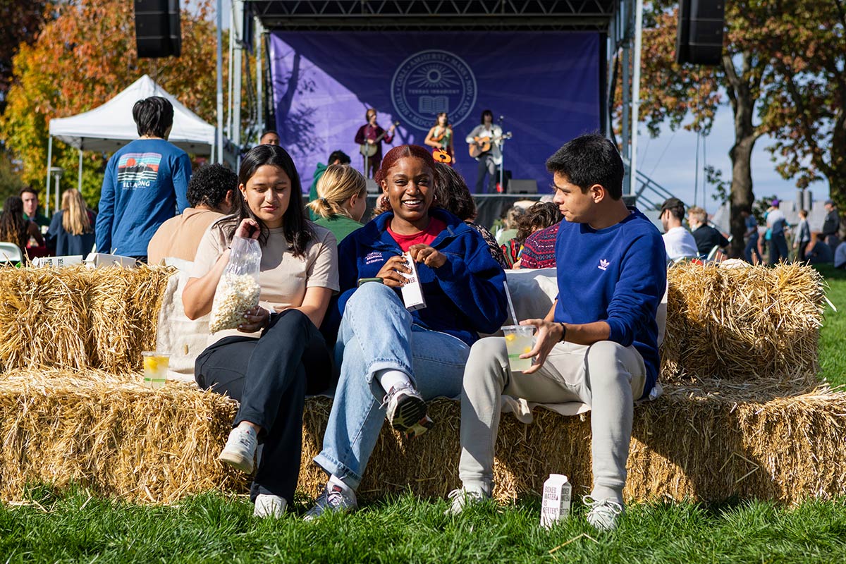 Three students sitting on hay bales, eating popcorn and drinking lemonade.