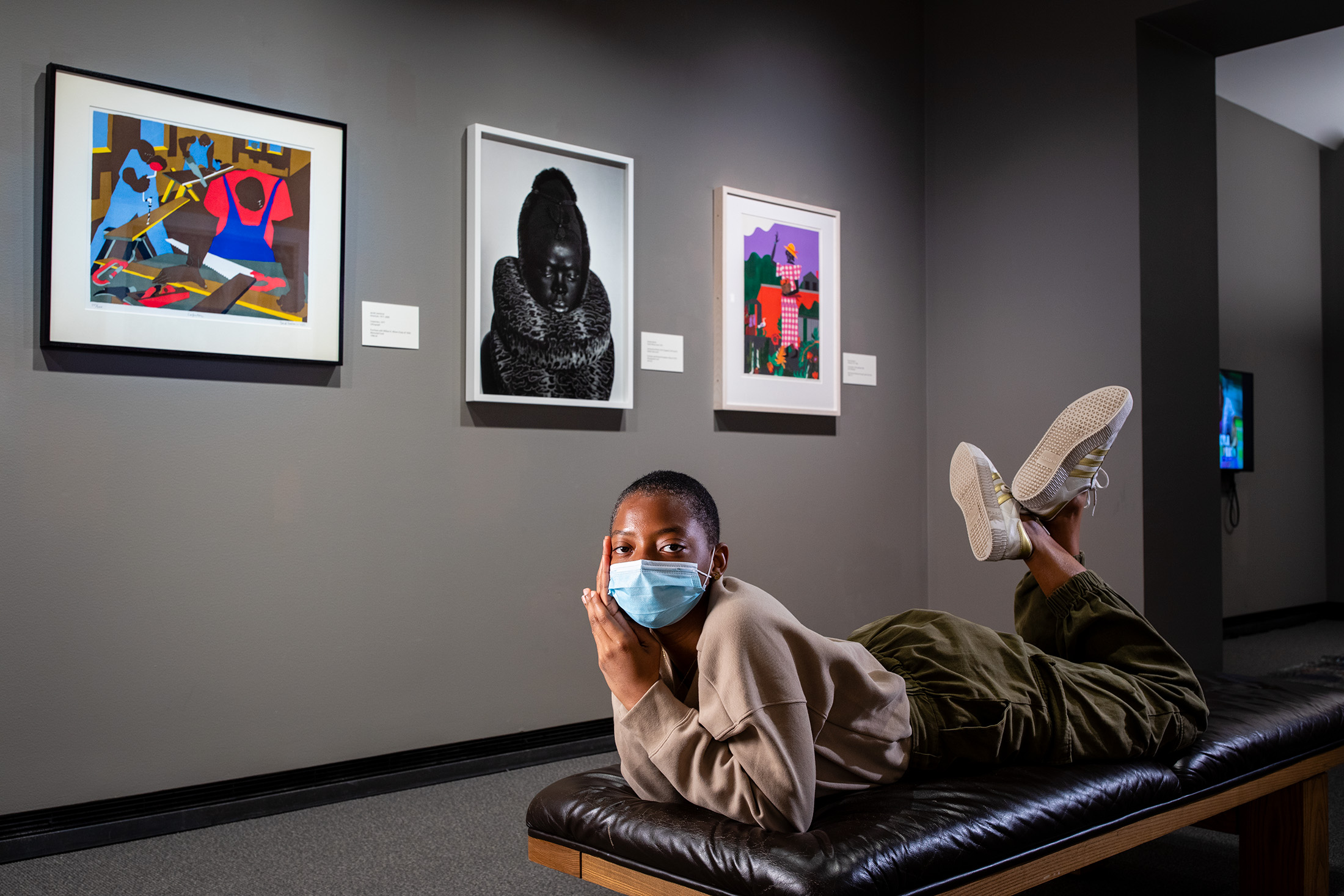 Melody Dodoo '21 wearing a mask and laying down in front of art hanging on a wall