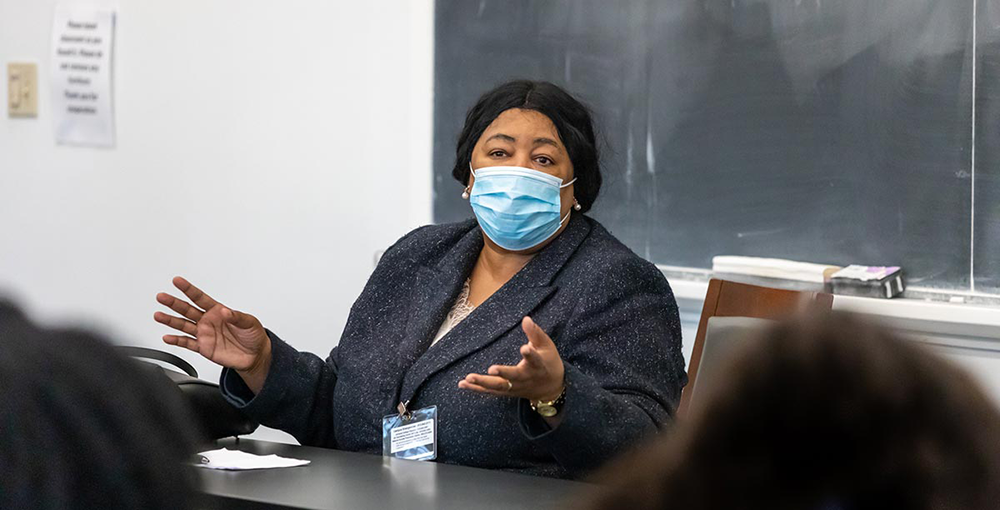 A photo of a woman wearing a mask and talking in a classroom