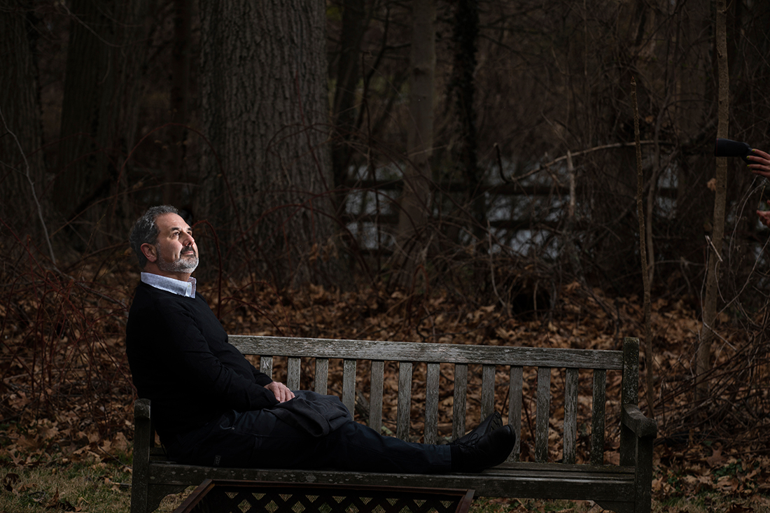 Marc Schultz reclines on a wooden bench outside.