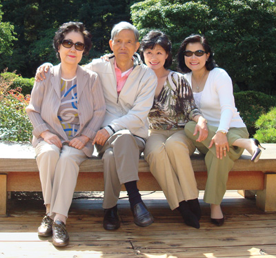 Thai Lee ’80 sitting on bench in her garden, surrounded by sister and father and mother