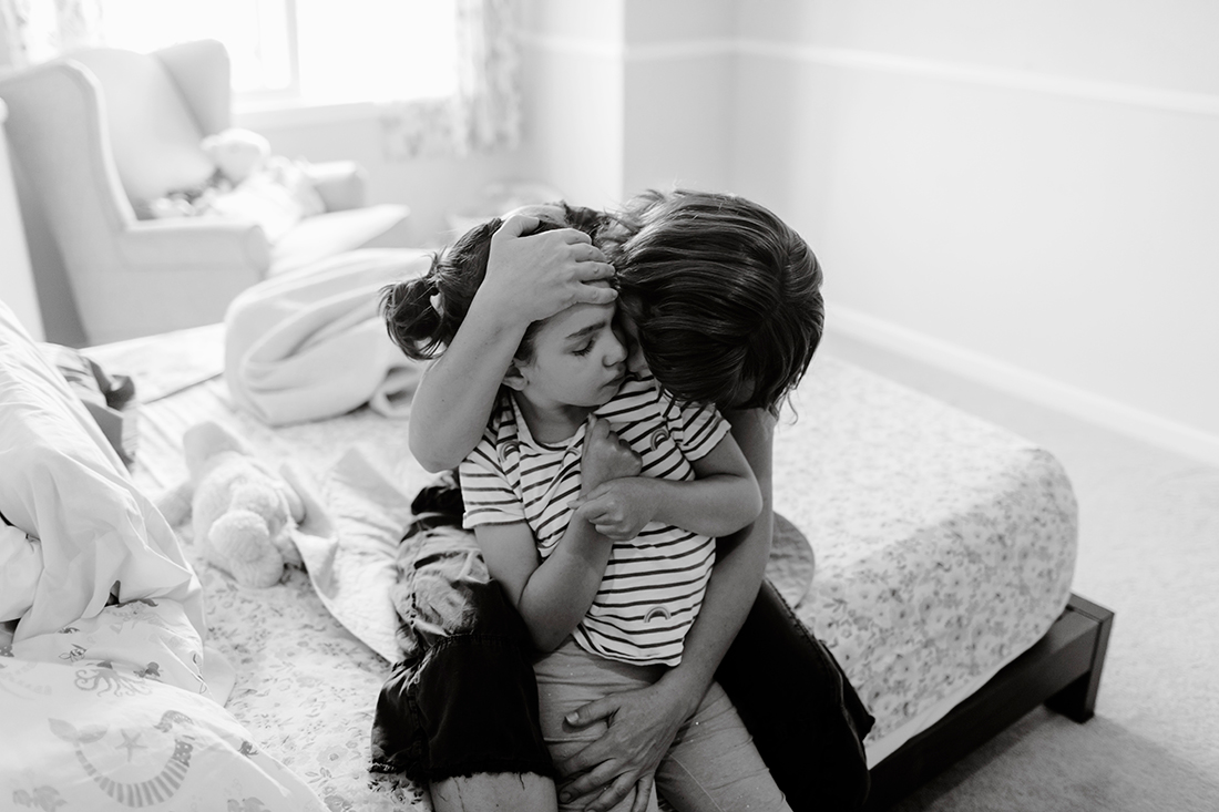  A black and white photo of a mother hugging a child on a bed