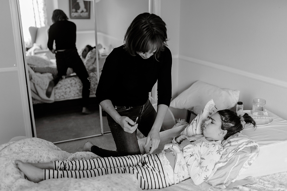 A black and white photo of of mother caring for a young girl lying on a bed