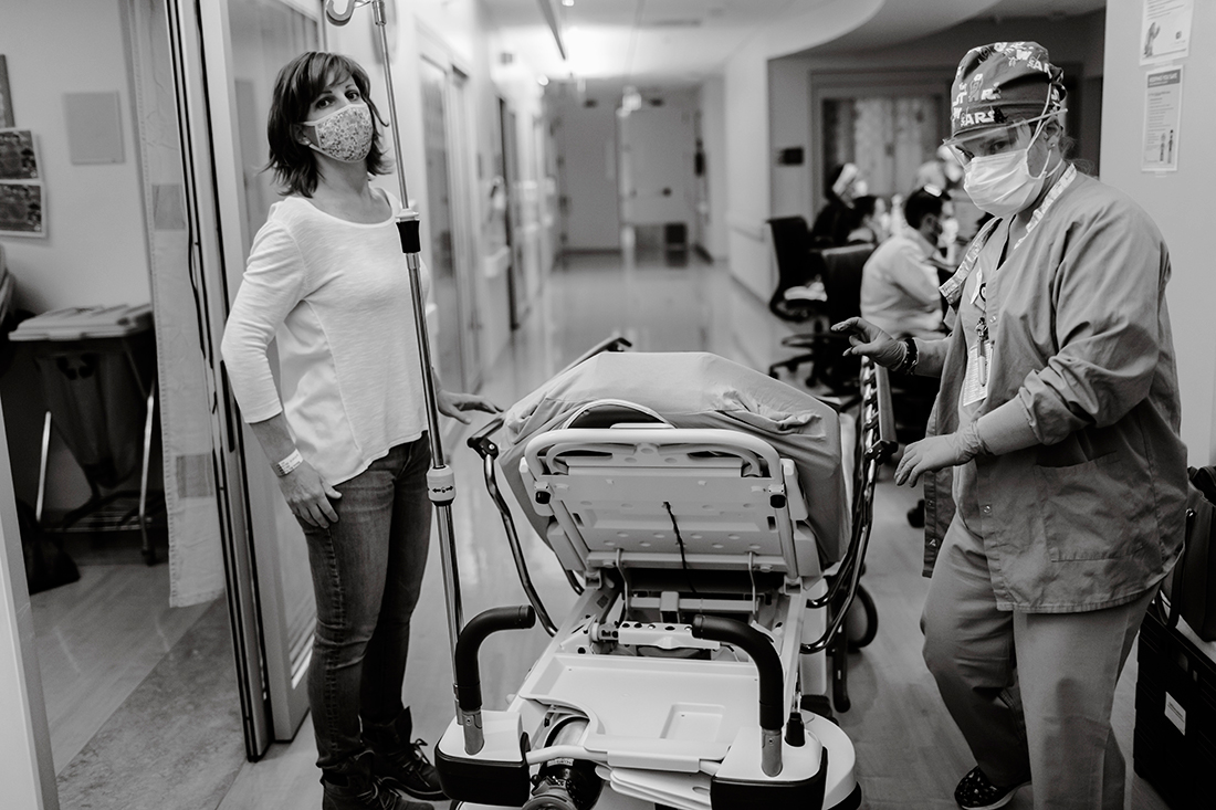 A black and white photo of a woman and a doctor standing next to a hospital bed in a hallway