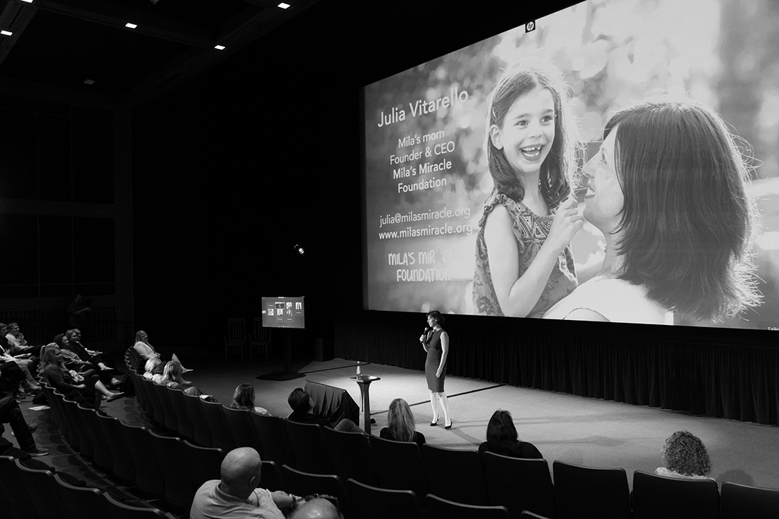 A black and white photo of a woman on stage giving a presentation to a large audience