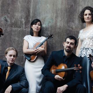 The Chiara String Quartet posing in front of a wall and holding their instruments