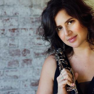 Closeup of Anat Cohen wearing a black blouse and holding her clarinet over her right shoulder