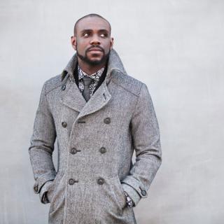 Omar Thomas standing with his hands in the pockets of his double-breasted gray coat