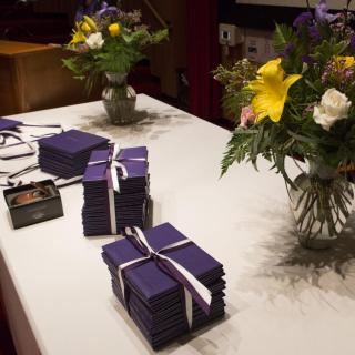 Stacks of prize certificate folders tied with ribbons and arranged on a table with vases of flowers 