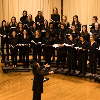Arianne Abela conducts singers standing on the Buckley Recital Hall stage