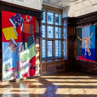 Installation shot of Rotherwas Project 5: Christopher Myers, The Red Plague Rid You for Learning Me Your Language. Quilts of many different fabrics and colors depicts scenes of Shakespeare's "The Tempest" and adorn the wood-paneled rooms of the Rotherwas Room.