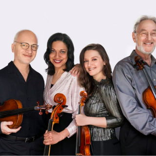 Juilliard String Quartet standing close together, smiling and holding their instruments