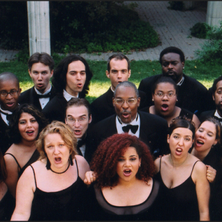 Dett Chorale gathered on a lawn, singing in black dresses and tails