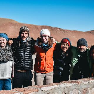 Students and Juan, the program director, in a mountainous setting, with arms on each other's shoulders.
