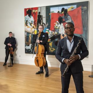 Anthony McGill and the Catalyst String Quartet holding their instruments, standing in a gallery in front of a brightly colored painting