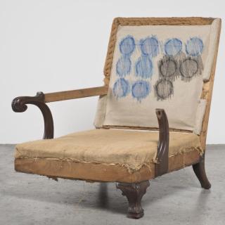 Sculpture of arm chair missing one leg and one arm; blue and black circle print on chair back. 