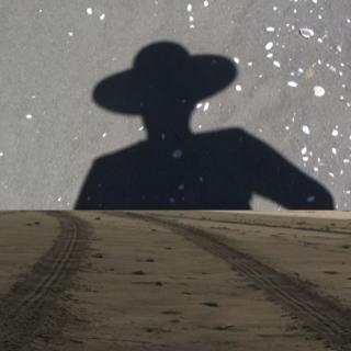 Illustration showing the shadow of a person wearing a wide-brimmed hat, beyond a landscape of dirt with tire tracks