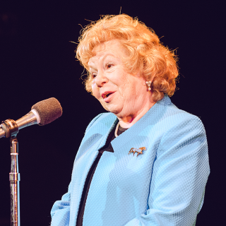 Henny Lewin at microphone in light blue jacket