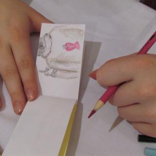 A pair of hands on a tabletop, holding a pink colored pencil and a hand-drawn flipbook
