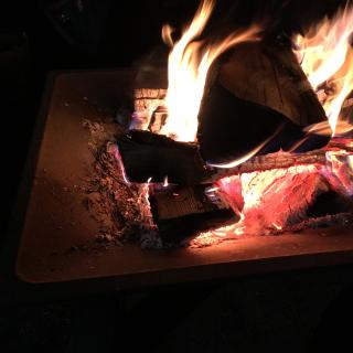 Image of a fire burning at night.  Logs glowing orange in a metal fire pit.