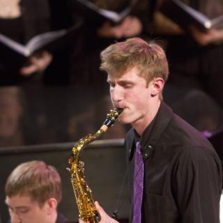 Closeup of Zach Yanes '17 playing the saxophone on stage in front of other musicians