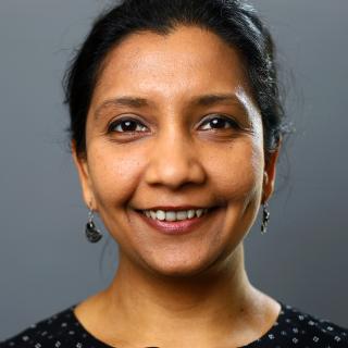 Headshot of Mansi Srivastava, wearing earrings and smiling as she looks into the camera