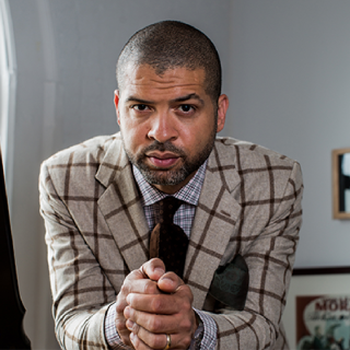 Jason Moran in plaid blazer and tie, leaning into the camera