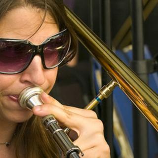 Closeup photo of Sara Jacovino wearing sunglasses and blowing into a trombone