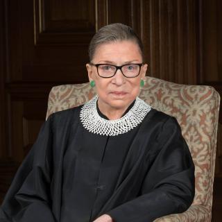 Image of Justice Ginsburg sitting in a chair wearing a scarlet robe (court attire)