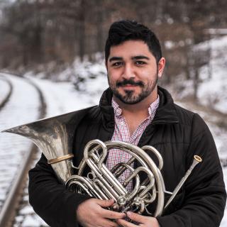 Patrick Williams '18 standing in front of snow-covered train tracks, holding his French horn