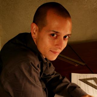 Closeup of Ryan Vigil leaning over a piano and sheet music, with a pair of eyeglasses in his hand