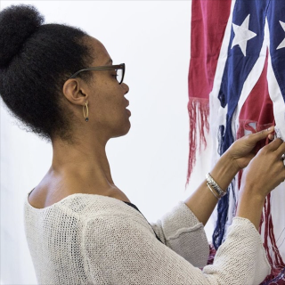 Sonya Clark unraveling a Confederate flag with her hands