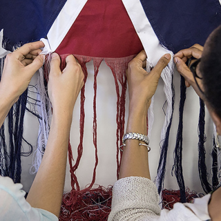 The arms and hands of two women as they unravel a Confederate flag