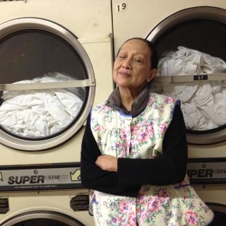 A woman standing in front of dryers full of laundry with her eyes closed and arms crossed