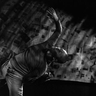 Black-and-white photo of Annie Wang dancing in front of a wall full of newspaper pages