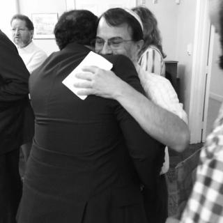 Black-and-white photo of two people embracing at a Roots Initiative social hour