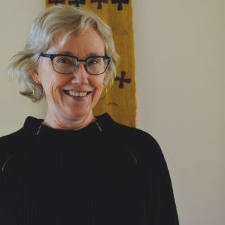 Catherine Ciepiela wearing a black sweater and eyeglasses and smiling at the camera
