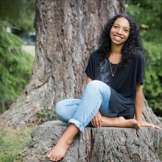 Lisbeth White, smiling as she sits barefoot at the base of a tree