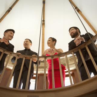 View from below of the Parker Quartet standing behind a curved railing and smiling at each other