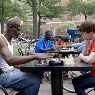 Still from "The Prison in Twelve Landscapes," showing people playing chess in a park