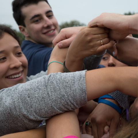 Students clasp hands in a group during an orientation activity