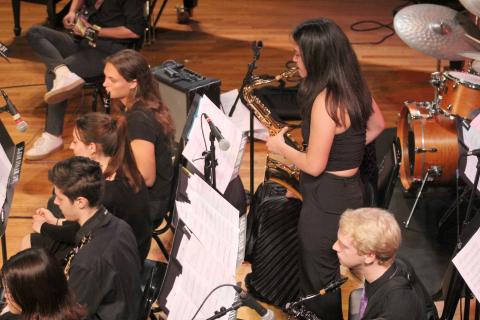 one student standing up and playing a saxophone solo amidst the band