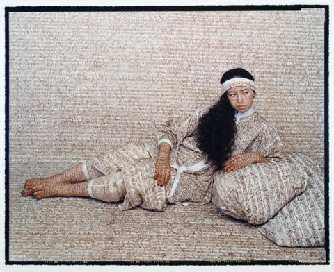 A woman with long dark hair leans on the ground.