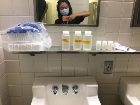 I take a mirror selfie with a layout of various bottles of river water on the counter of the bathroom