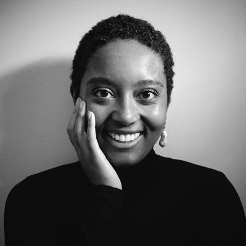 A black and white photo of a smiling Black woman with her hand on her cheek