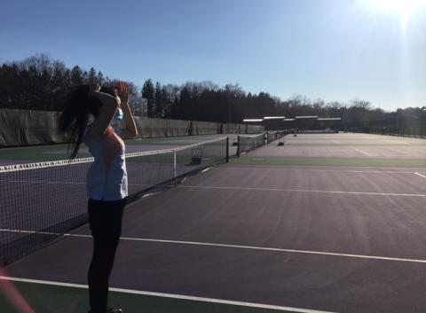 Empty tennis courts except my friend who is facing away, tying up her hair