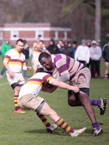 Amherst College player charges through a tackle from Williams