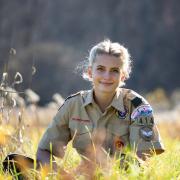 A woman in an Eagle Scout uniform sitting in a field and smiling at the camera