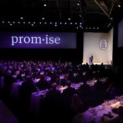 A large stage in purple light with the word "promise" projected on a big screen